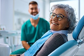 Woman with black glasses smiling while sitting in treatment chair