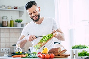 Smiling man preparing salad in kitchen