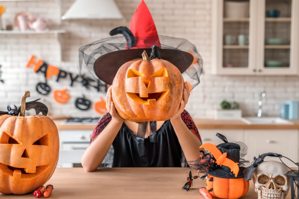 Woman in witch costume holding up carved pumpkin