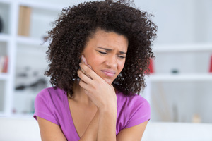 Woman in purple shirt with jaw pain due to TMJ disorder