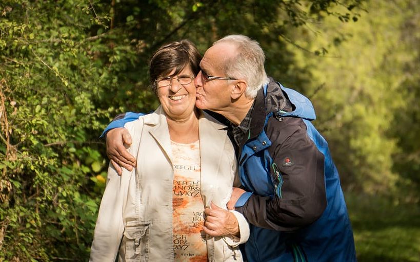 older person with dentures kissing partner on cheek 